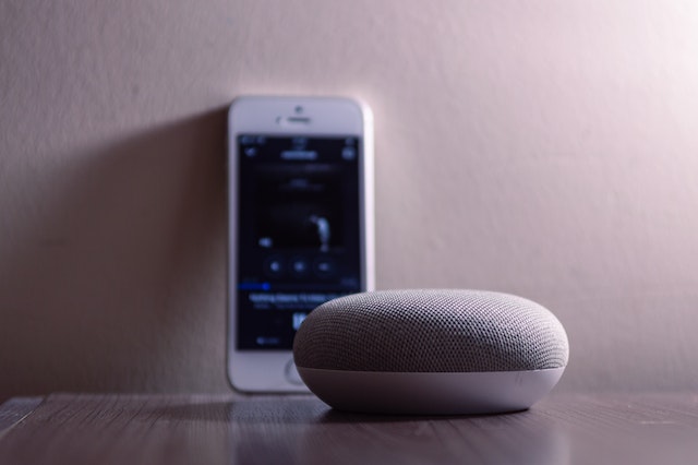 A smartphone device sits behind a Google smart speaker.