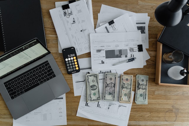 Bills, cash, and a laptop sitting on top of a work desk