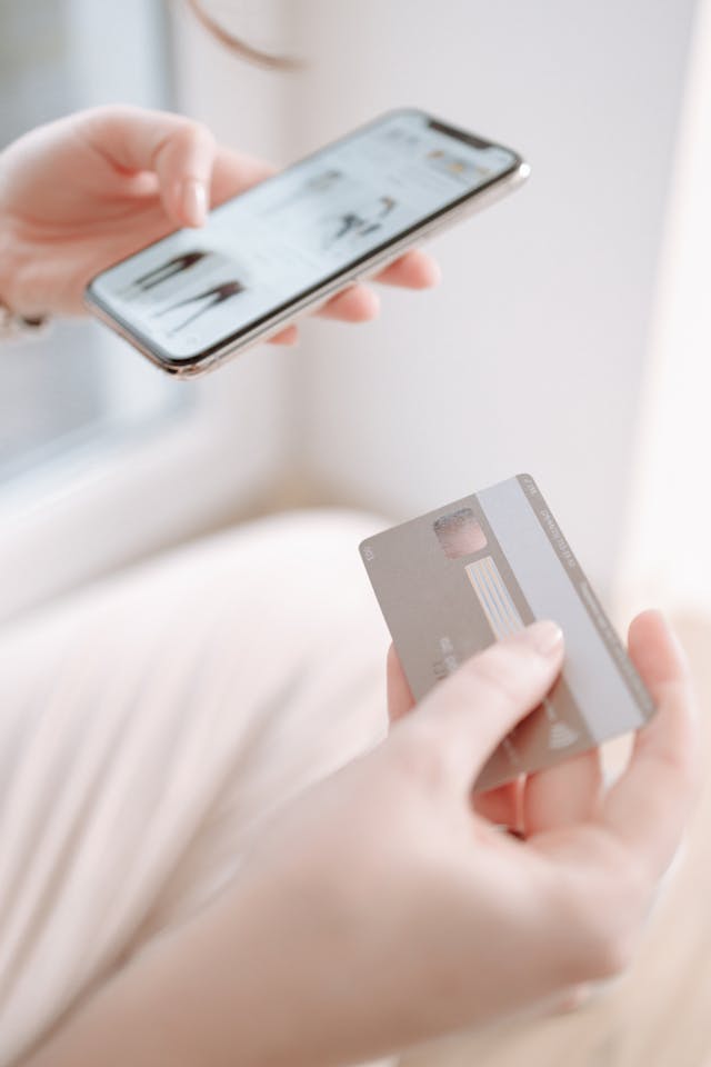 A person holding their phone and credit card to an online shop.